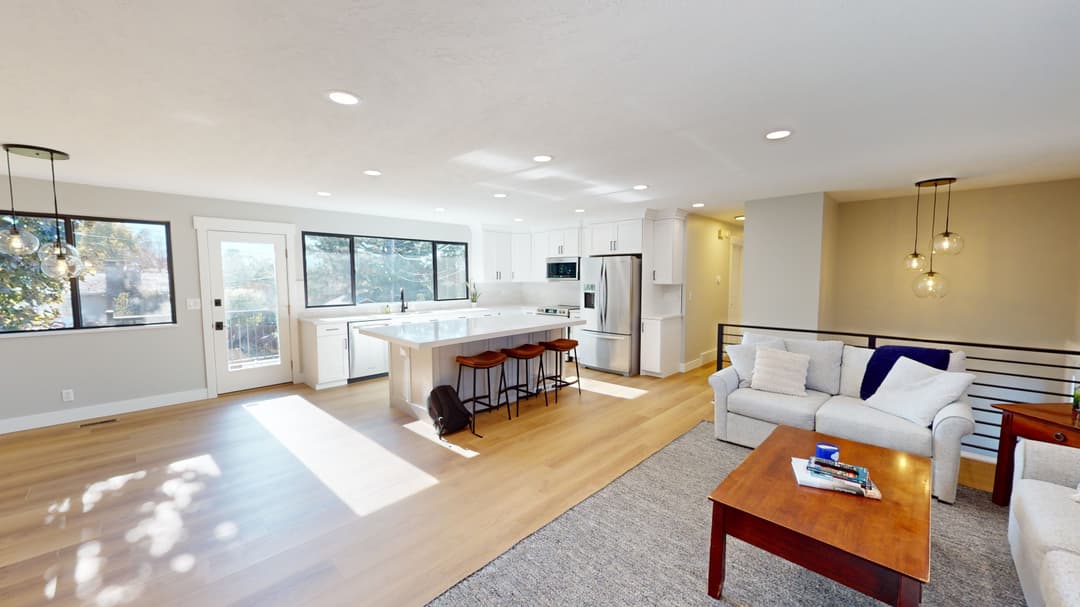 Spacious modern living room and kitchen with natural light, wooden floors, and stylish decor.