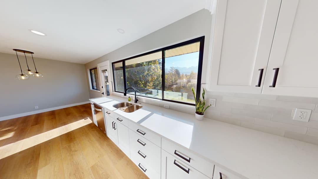 Modern kitchen with white cabinets, large window, and natural light highlighting the space.