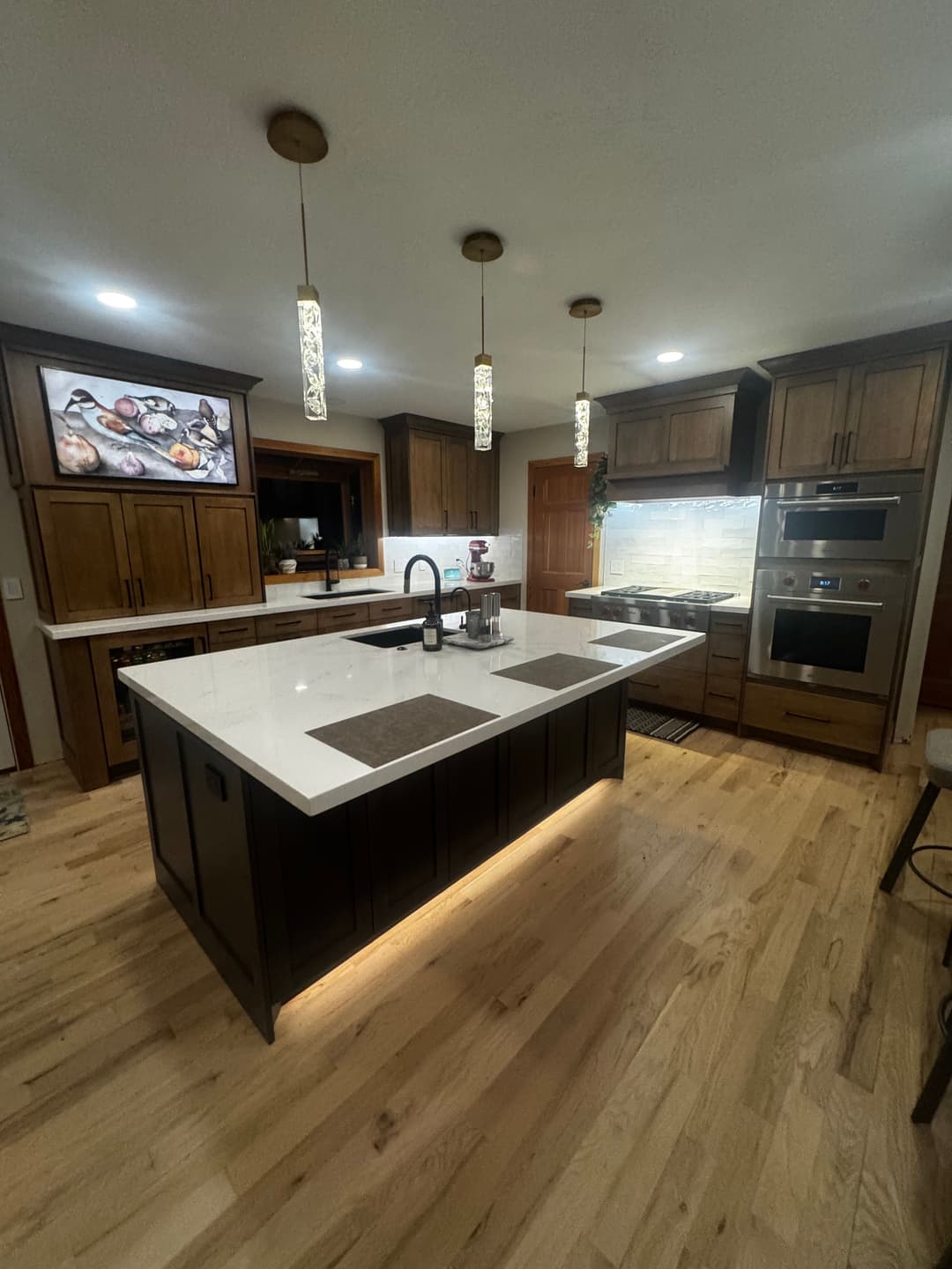 Modern kitchen with wooden cabinetry, white quartz island, pendant lights, and sleek appliances.