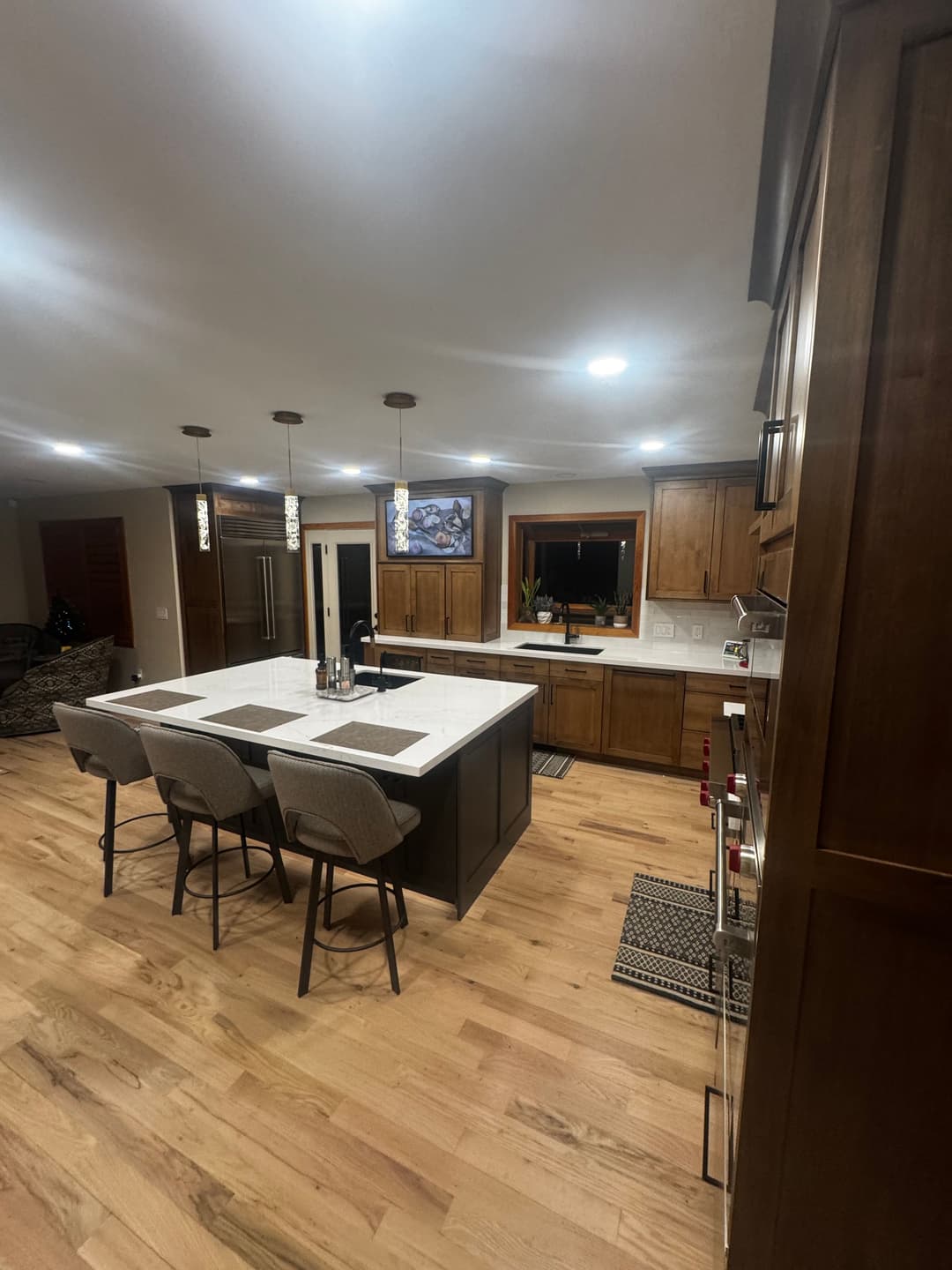 Modern kitchen with wooden cabinets, large island, and contemporary bar stools. Bright lighting.