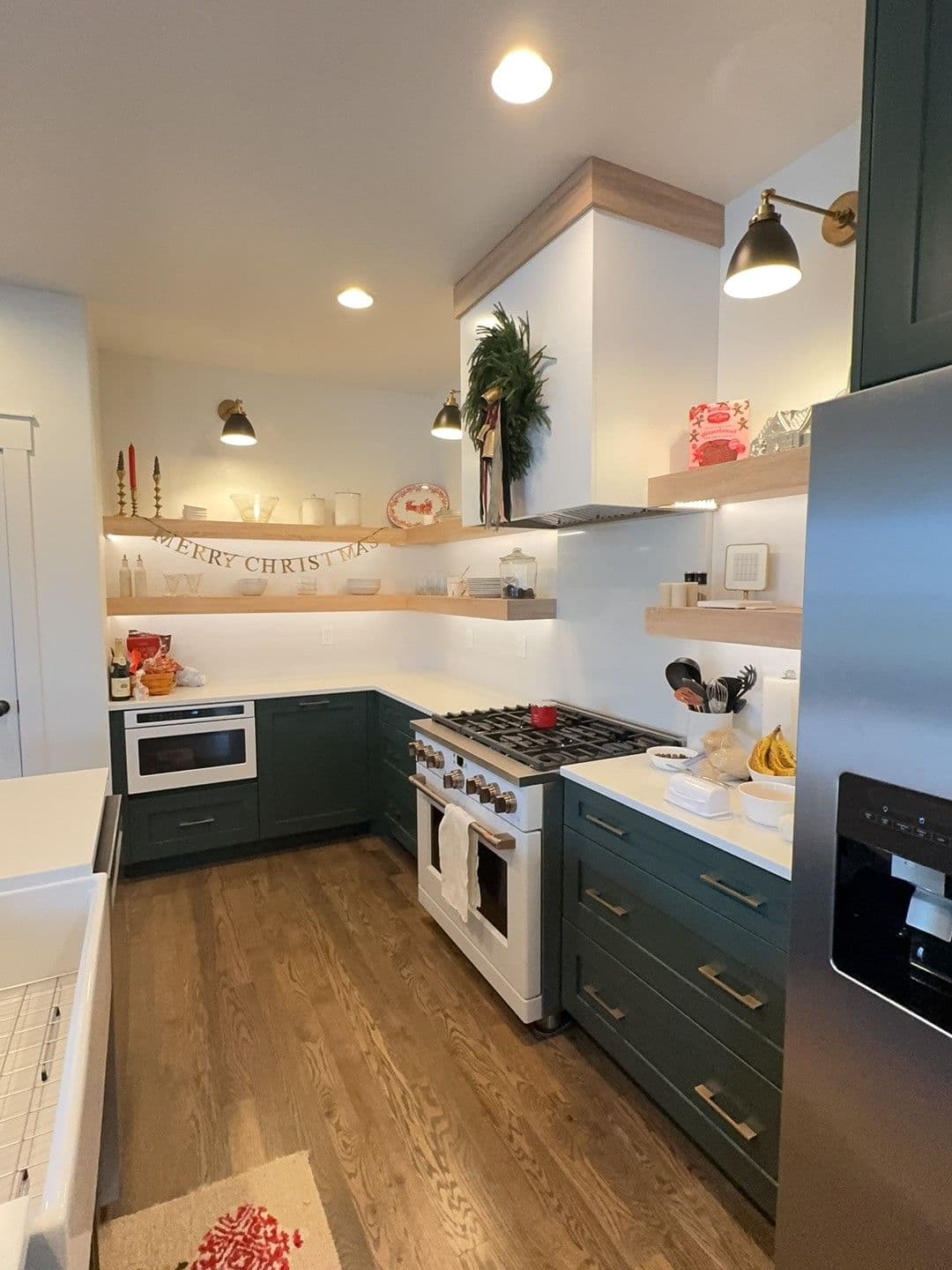 Modern kitchen decorated for Christmas with green cabinets, white countertops, and festive accents.