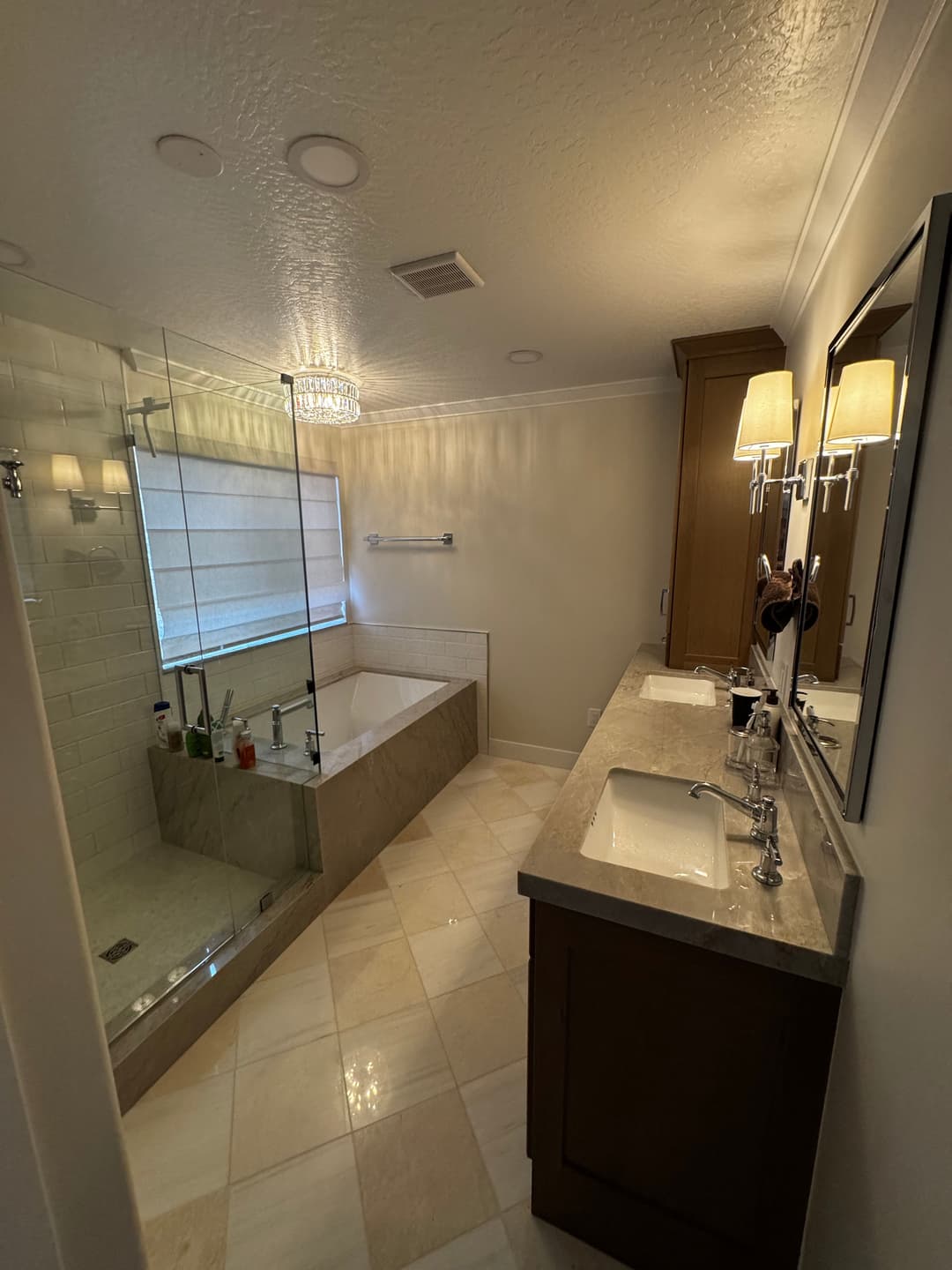 Modern bathroom featuring a glass-enclosed shower, bathtub, dual sinks, and elegant lighting.