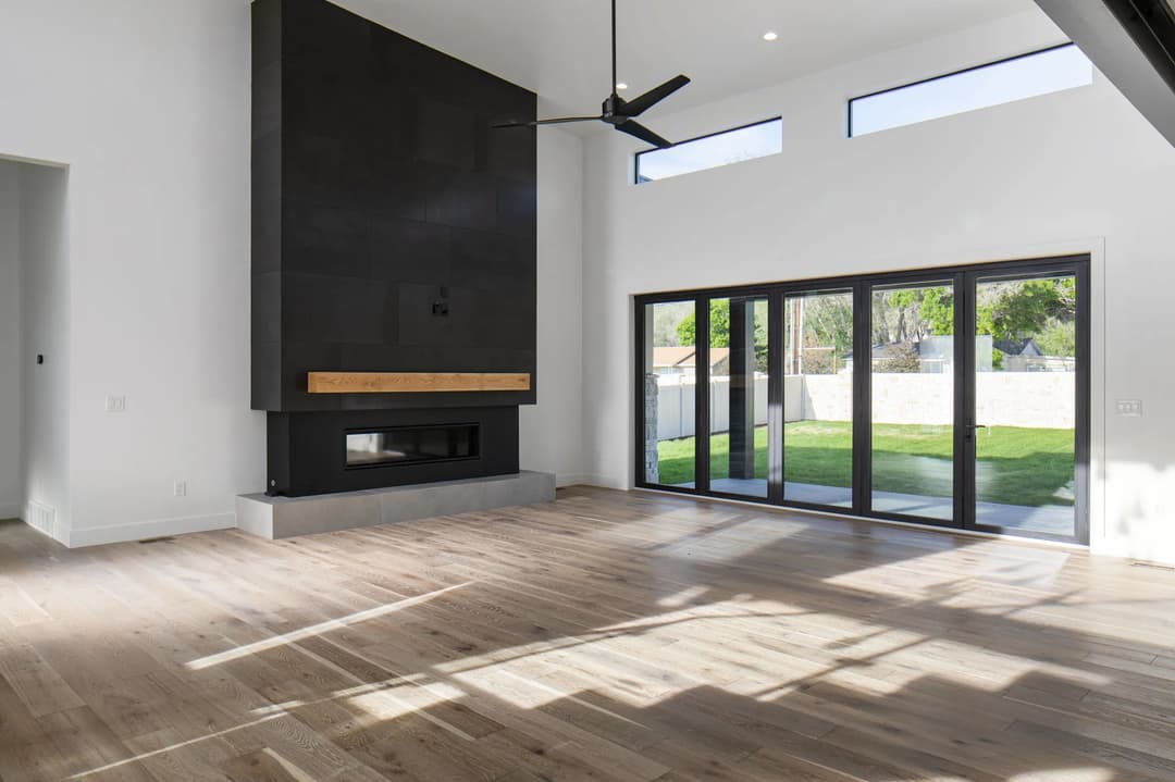 Modern living room with large windows, natural light, and a sleek black fireplace.