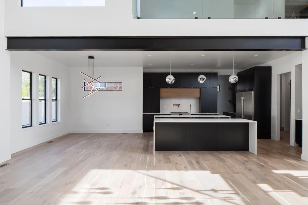 Modern kitchen with sleek black cabinetry, island, pendant lights, and natural light from windows.