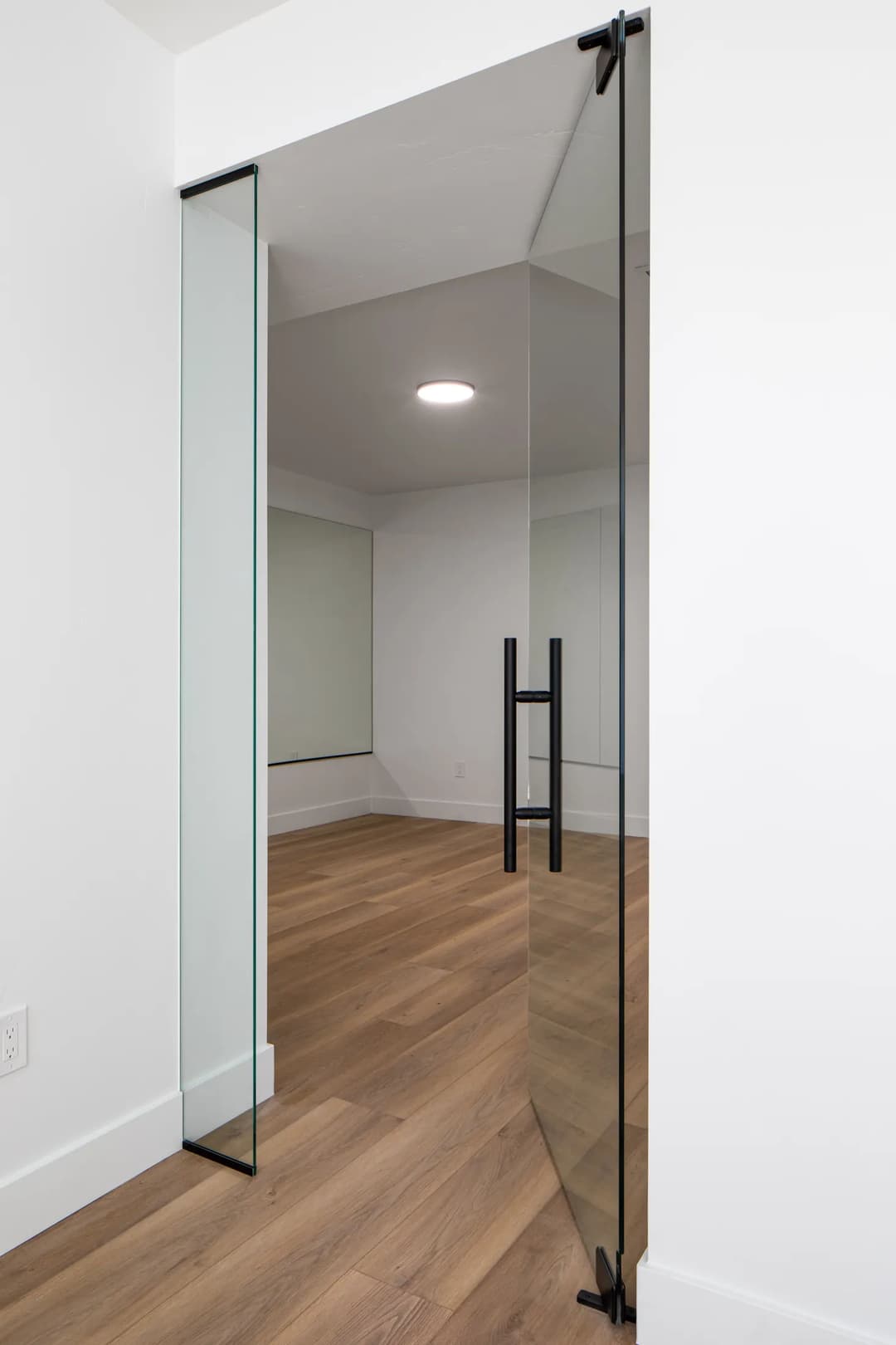 Modern glass door entrance with sleek black handles and wooden flooring in a bright room.