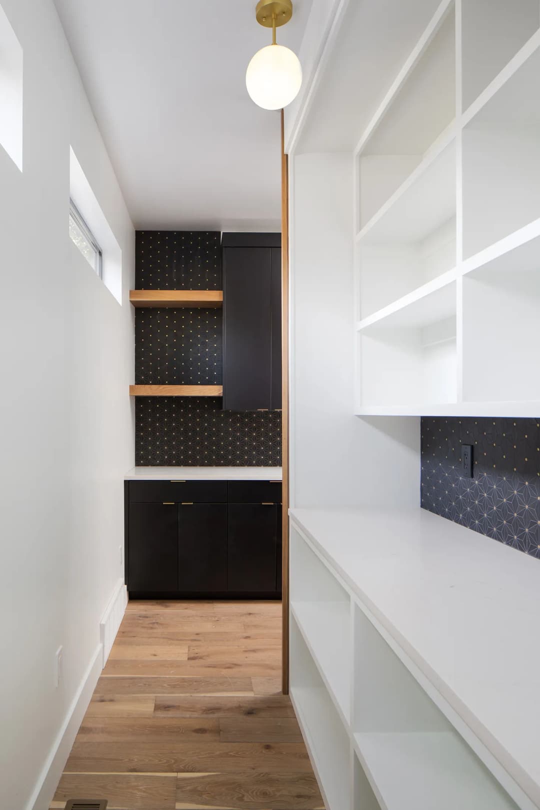 Modern hallway with white shelves, black cabinets, and a gold pendant light accent.