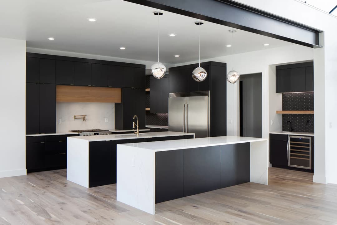 Modern kitchen with black cabinetry, white island, pendant lighting, and stainless steel appliances.