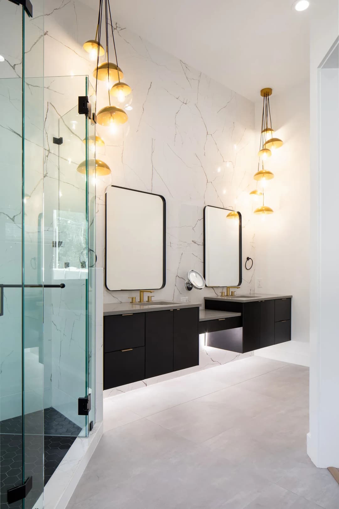 Modern bathroom with dual sinks, elegant lighting, and glass shower featuring marble walls.