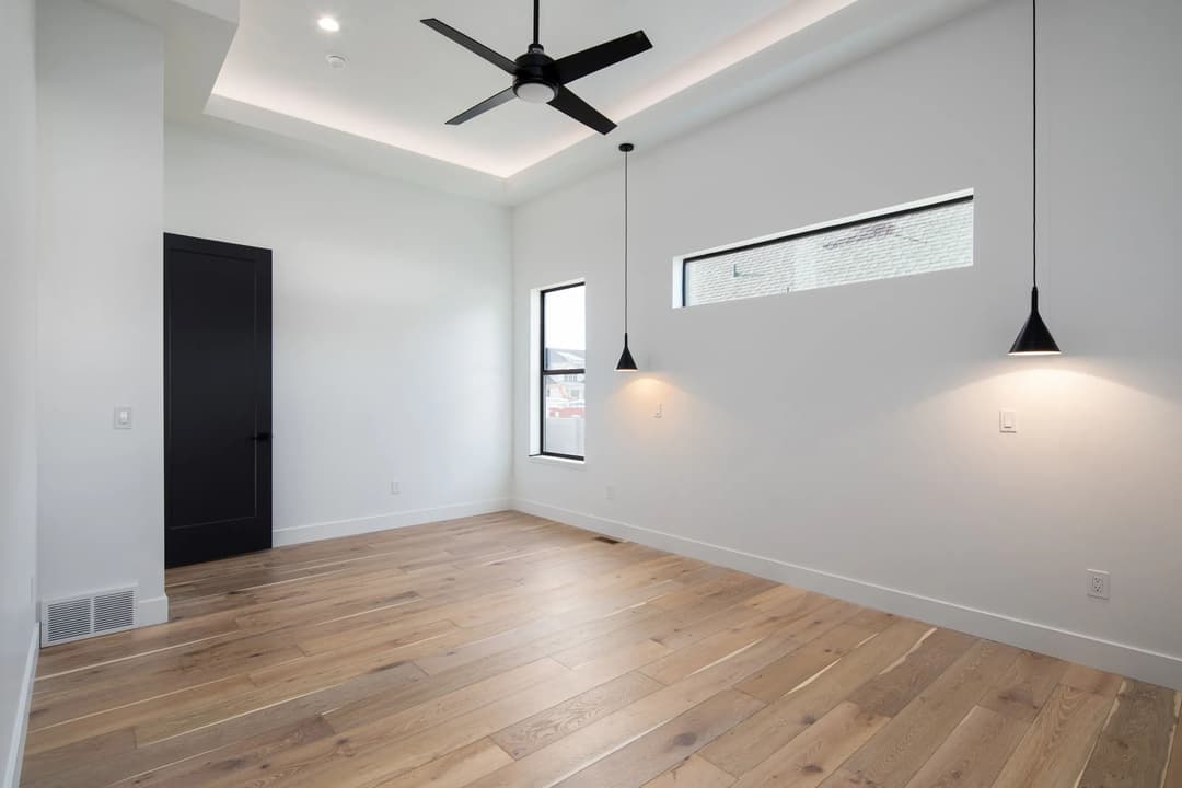 Modern empty room with wooden flooring, ceiling fan, and stylish pendant lights.