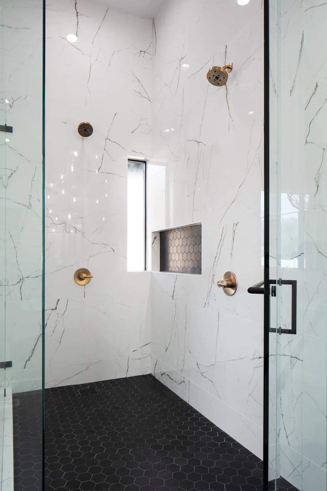 Modern shower with white marble walls, hexagon floor tiles, and brass fixtures.