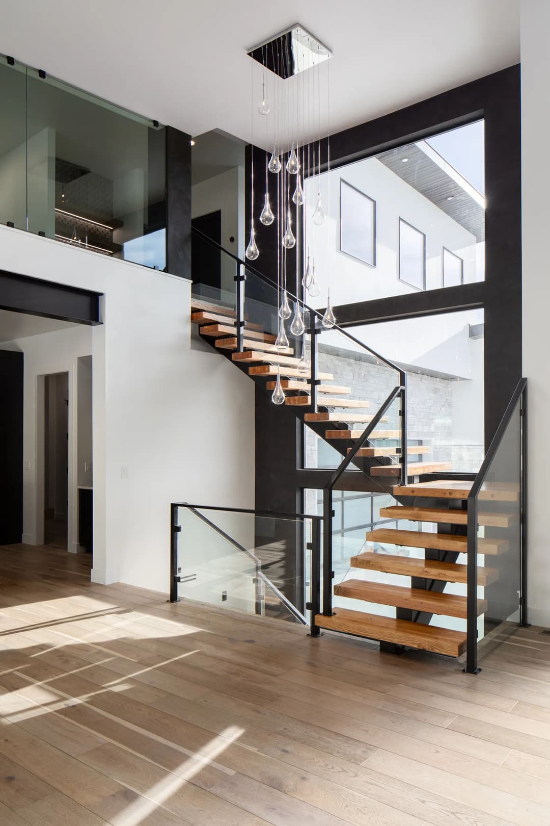 Modern interior featuring a stylish wooden staircase, glass railing, and contemporary lighting fixture.