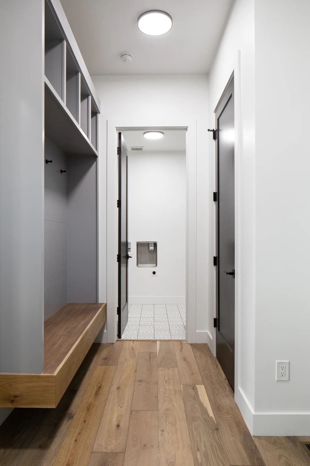 Modern hallway with wooden flooring, gray cabinetry, and two doors leading to a laundry area.