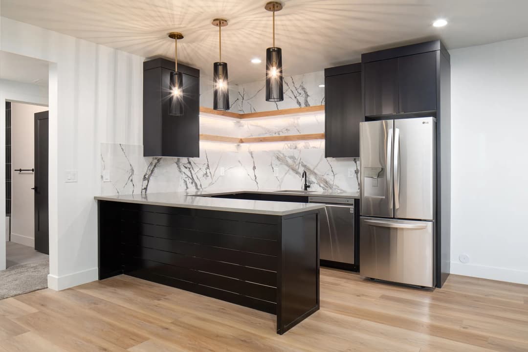 Modern kitchen with black cabinets, marble backsplash, pendant lights, and stainless steel appliances.