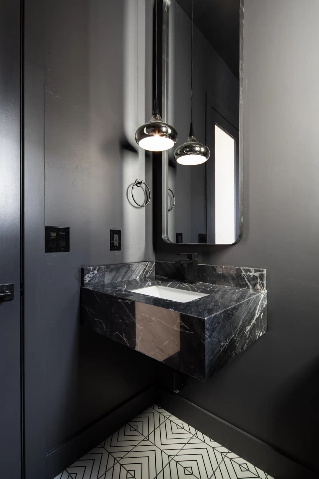 Modern black marble bathroom vanity with sleek mirrors and pendant lighting.