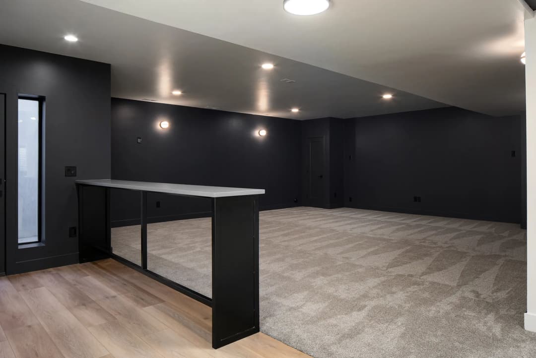 Spacious modern room with dark walls, soft carpeting, and stylish lighting. Ideal for versatile use.