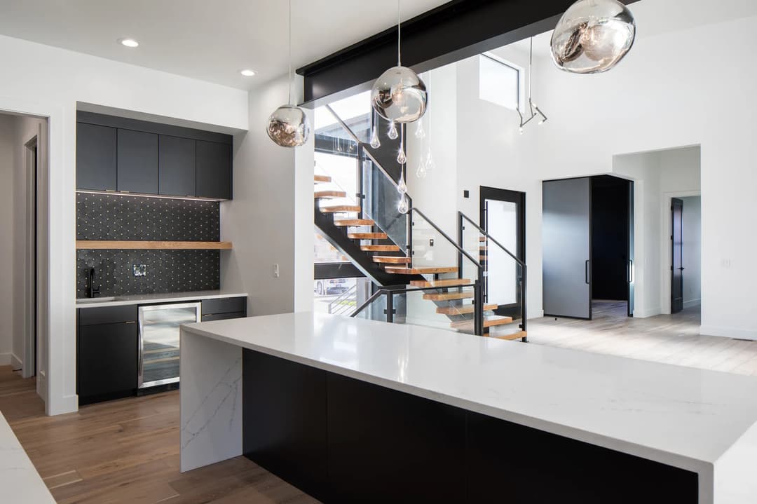 Modern kitchen with island, black cabinetry, and sleek pendant lighting near a staircase.