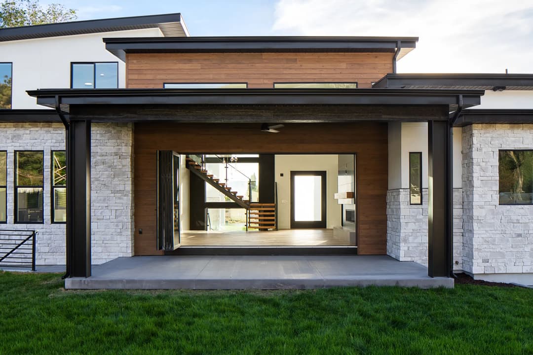 Modern house exterior with wooden accents, large windows, and covered patio on green lawn.