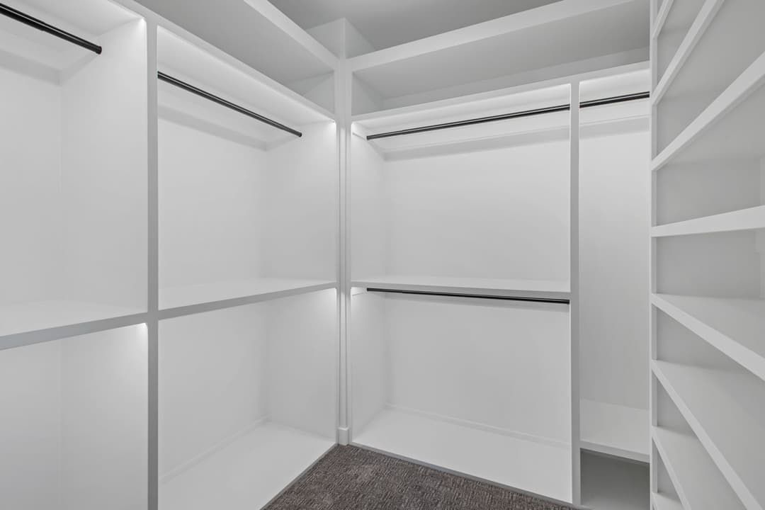 Spacious, modern walk-in closet with white shelving and hanging rods, well-lit design.