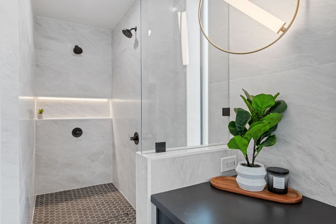 Modern bathroom featuring a glass shower, marble tiles, and stylish decor with potted plant.