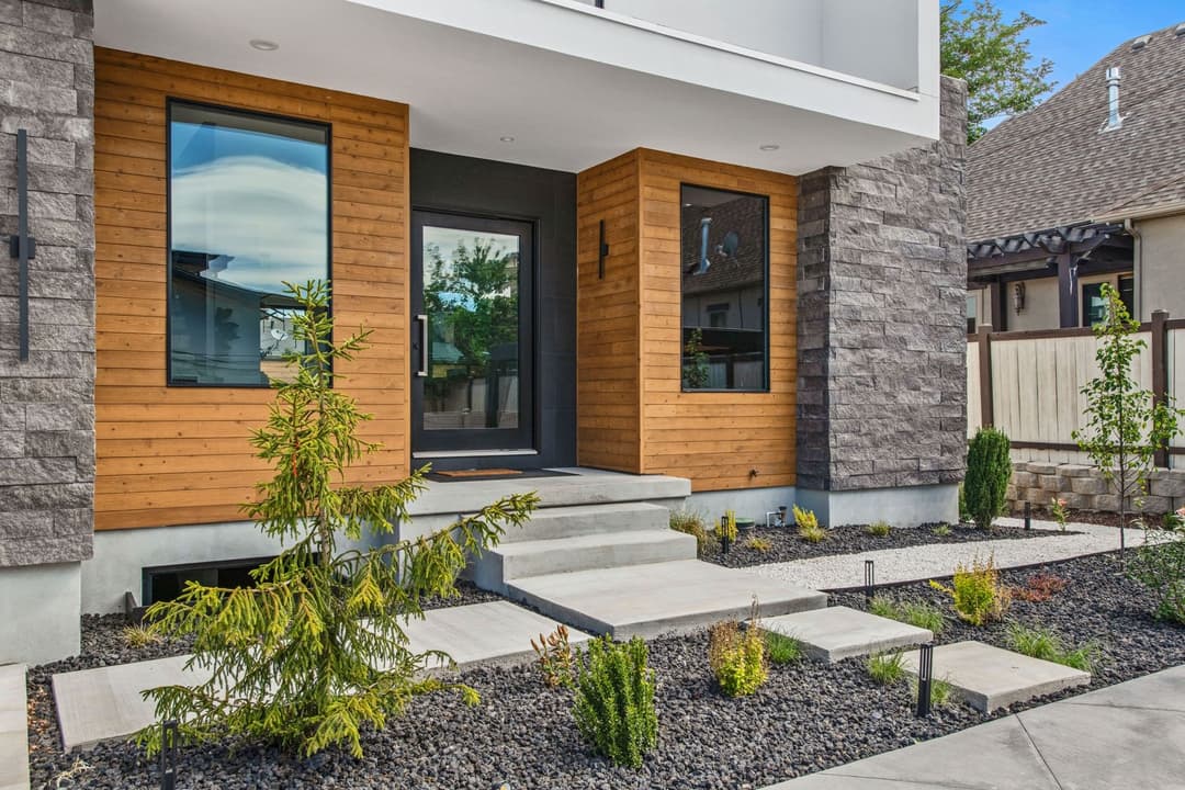 Modern home entrance featuring wood siding, large windows, and landscaped pathway.