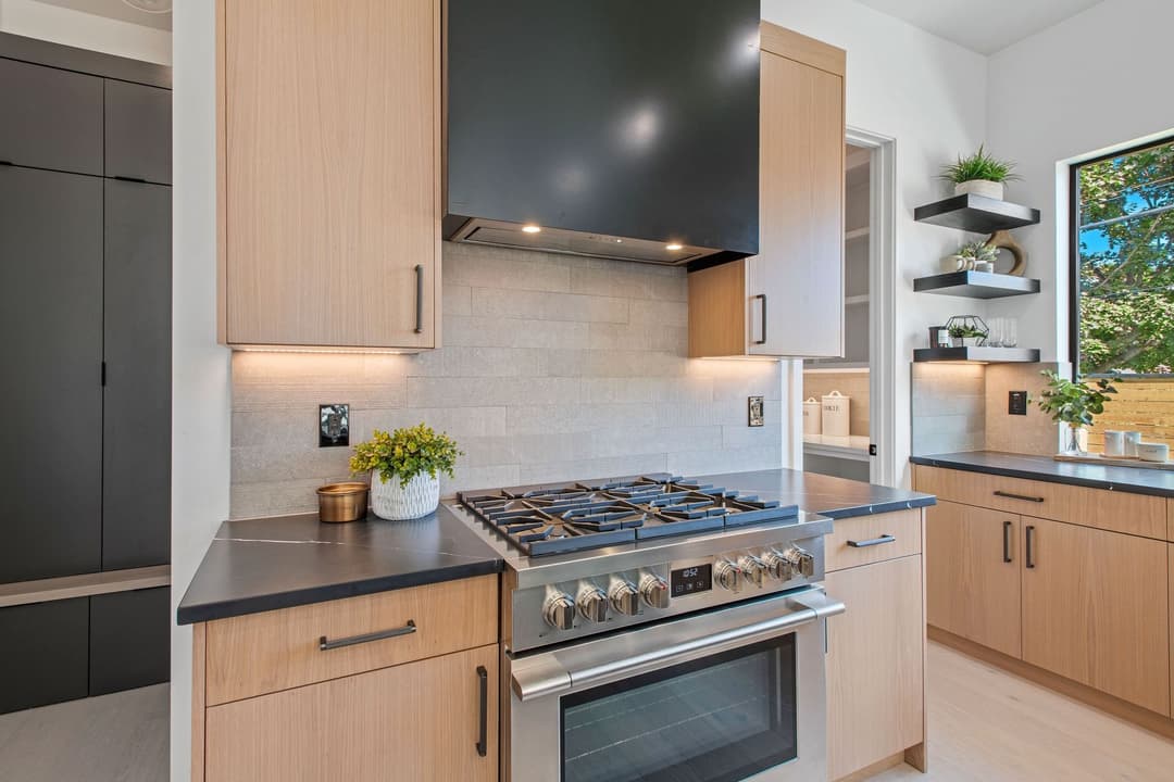 Modern kitchen with stainless steel range, wooden cabinetry, and sleek black countertops.
