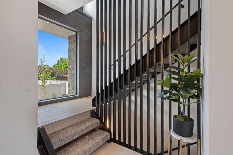 Modern staircase with black railing, plush steps, and a potted plant in a contemporary home.