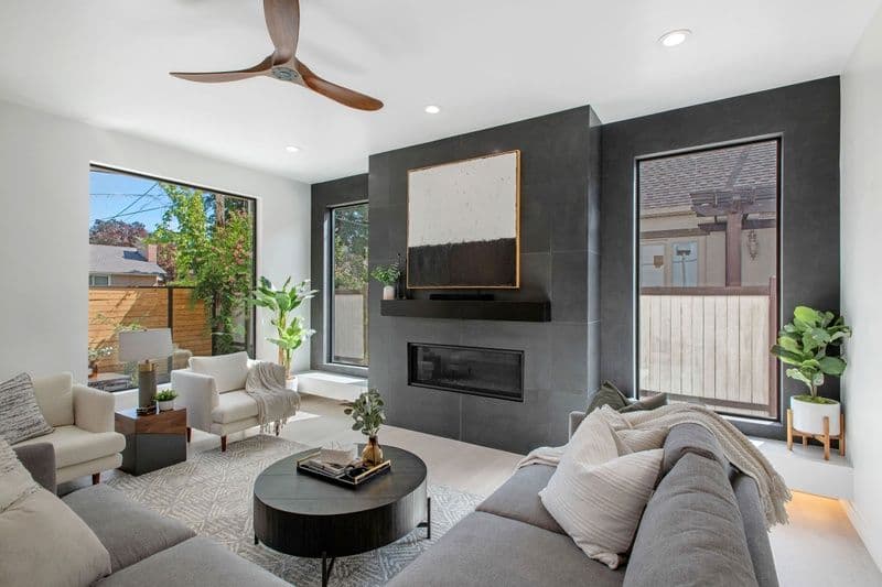 Modern living room with gray sectional, black fireplace, large windows, and stylish decor.