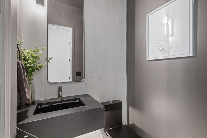 Modern bathroom with black sink, sleek mirror, and minimalist decor on gray walls.