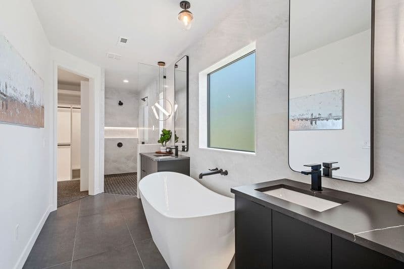 Modern bathroom with freestanding tub, sleek black fixtures, and natural light from large window.