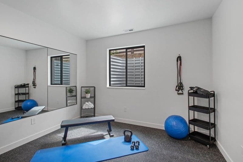 Home gym with workout equipment, blue exercise ball, bench, and mirrored wall.