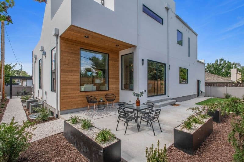 Modern home exterior with wooden accents, patio furniture, and landscaped garden area.