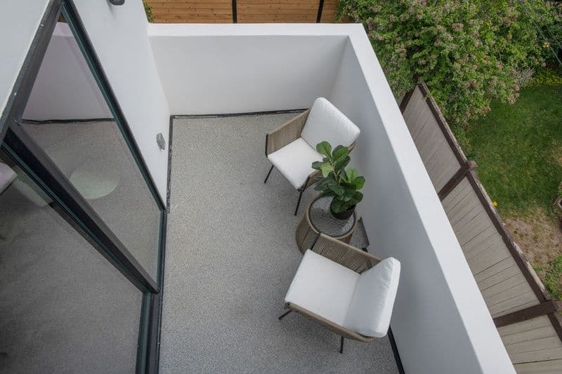 Modern balcony with two chairs and a potted plant, overlooking greenery.