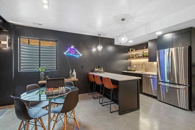 Modern kitchen and dining area featuring sleek black cabinets, pendant lights, and a neon sign.