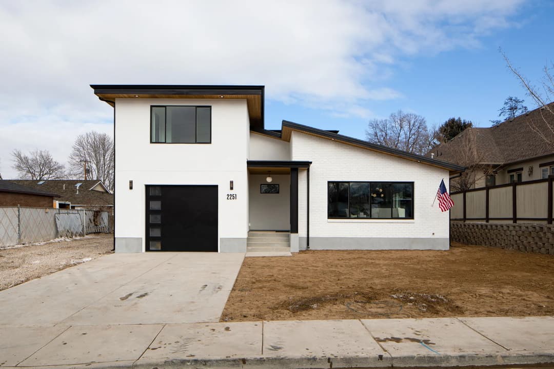 Modern two-story white house with black accents, large windows, and American flag in front yard.