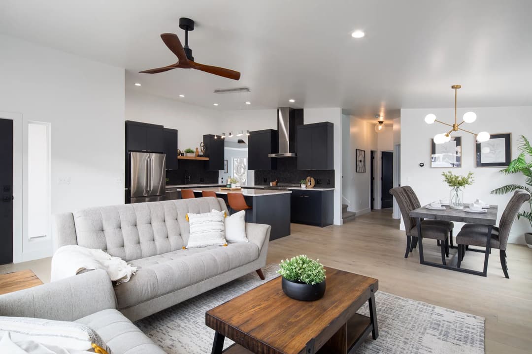 Modern open-concept living room with gray sofa, wooden dining table, and sleek kitchen design.