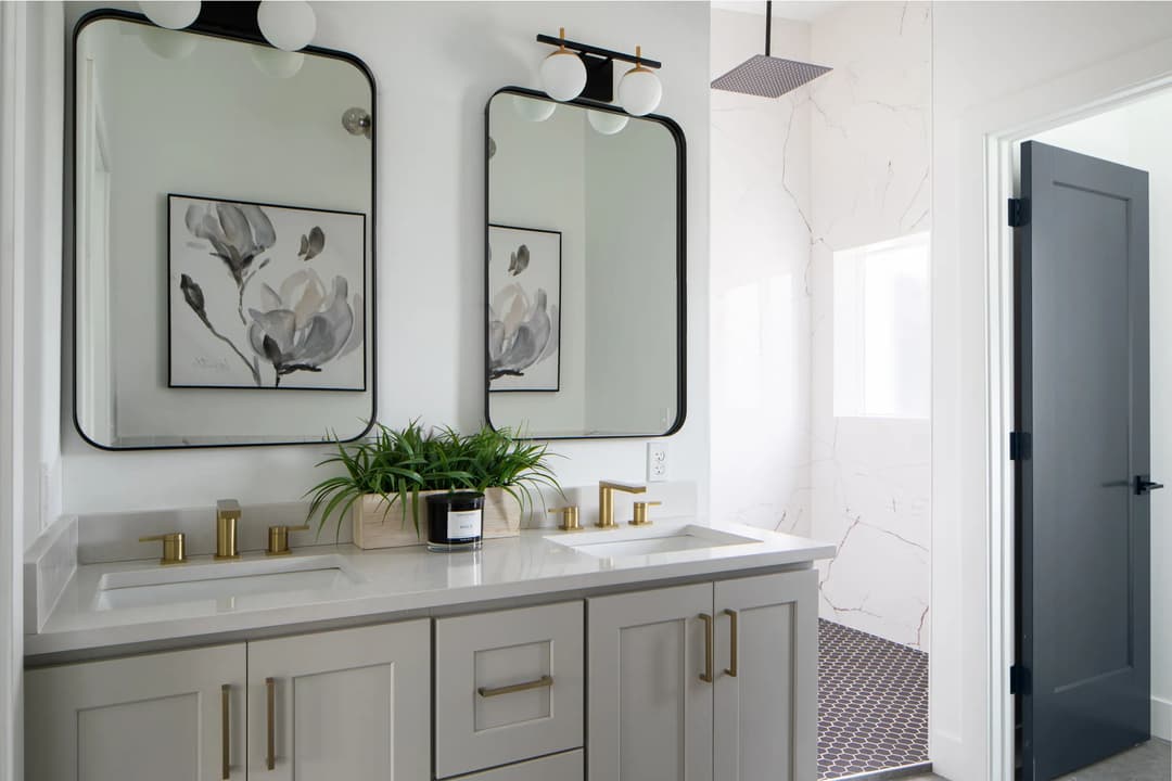 Modern bathroom with double sinks, elegant mirrors, and stylish decor featuring a plant.