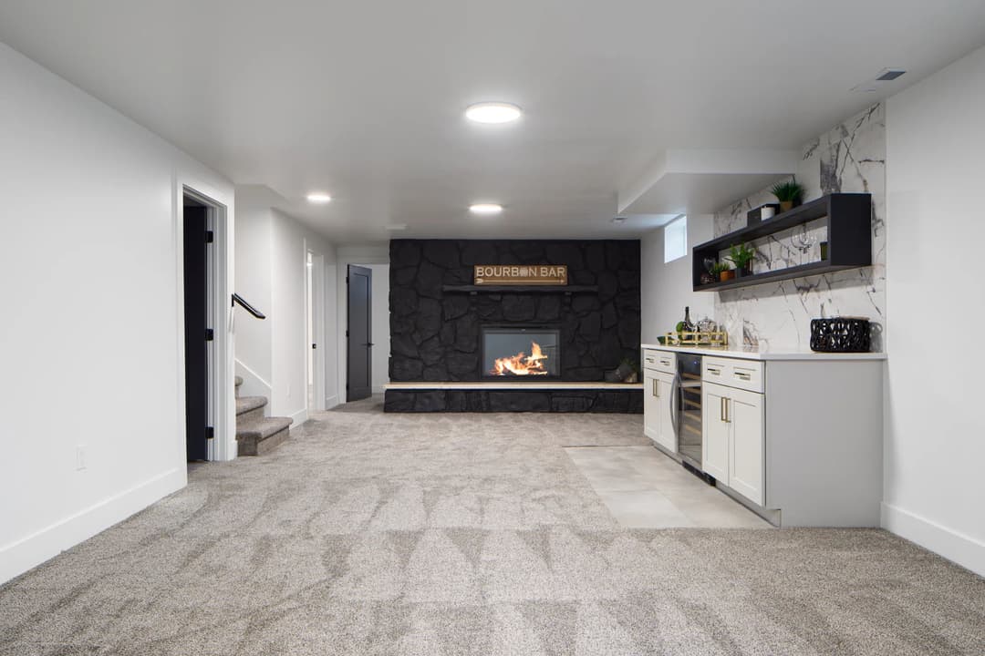 Modern basement with a Bourbon bar, fireplace, and stylish decor. Soft carpeting throughout.