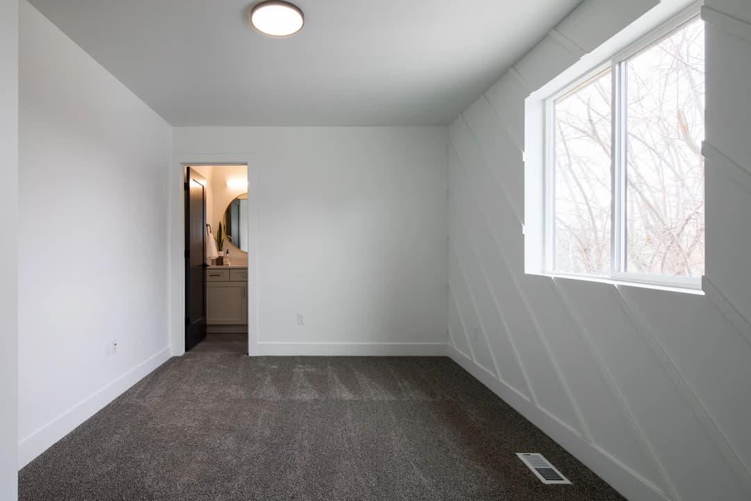 Modern bedroom with gray carpet, natural light, and adjacent bathroom entrance.