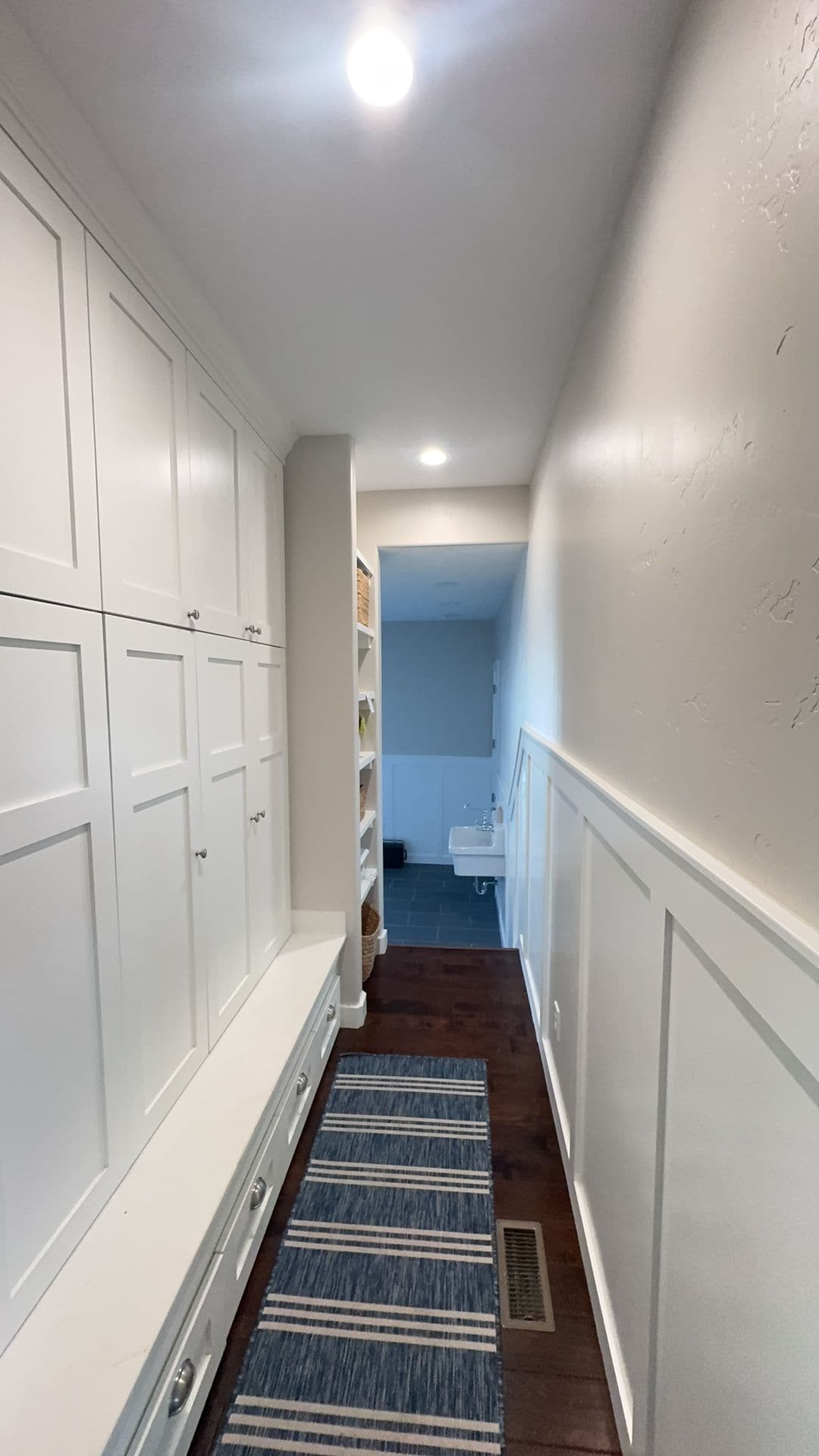 Modern hallway with white cabinetry, wooden flooring, and blue striped runner rug.